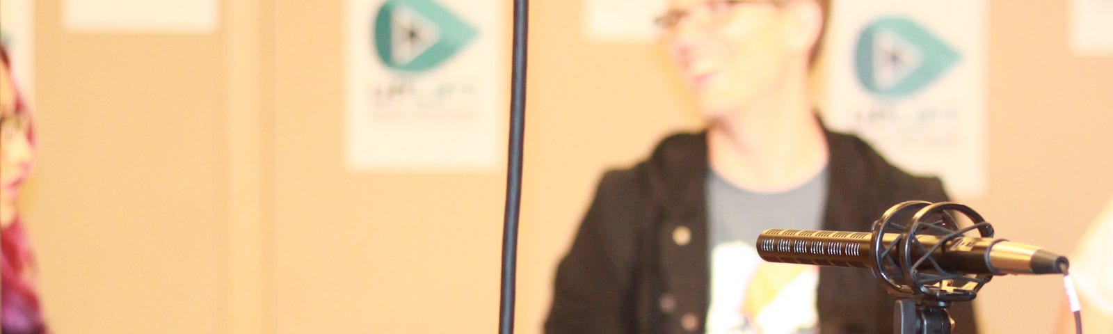 A blurred image of a creator speaking at a panel, with a camera in focus in the foreground.