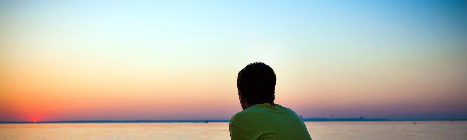 A lonely man sitting on a beach at sunset