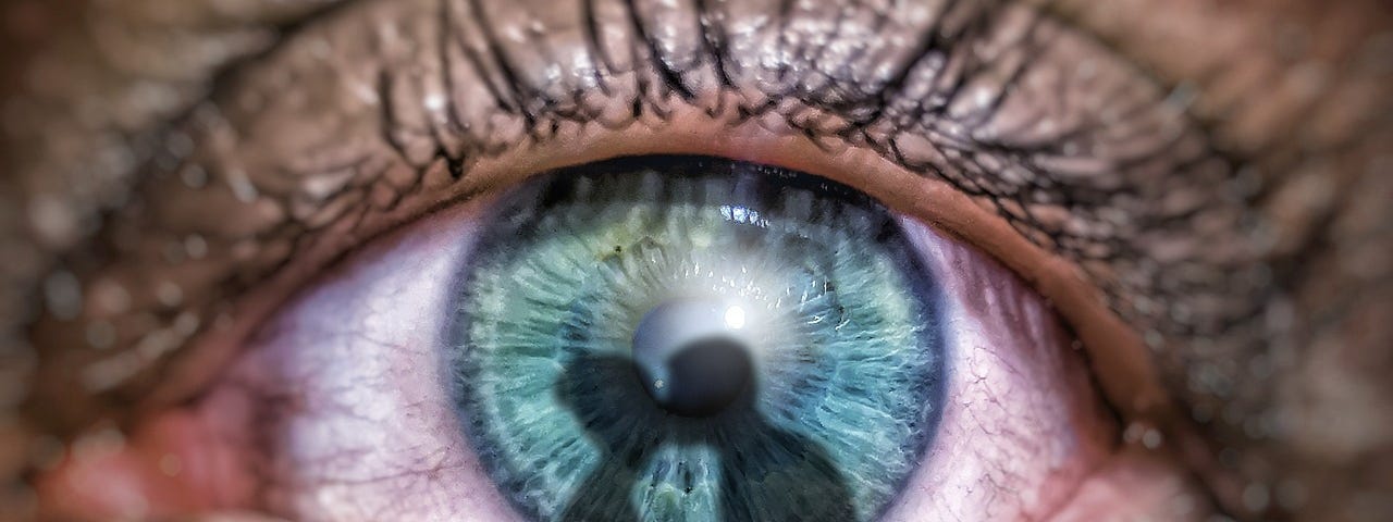 Closeup of a single blue tearing eye. On the iris of the eye is the shadow of a couple embracing, perhaps causing the sadness.