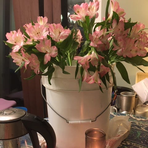 White bucket with light pink flowers in it. Teapot at left, and candle at right, forefront.