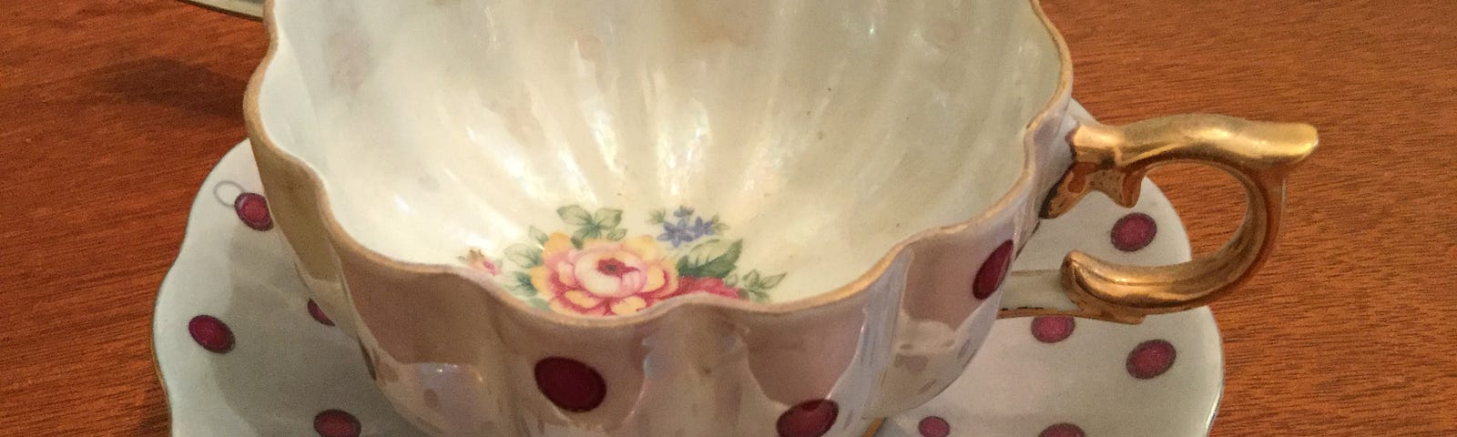 A vintage cup and saucer with gilt edges and a red polka dot pattern.