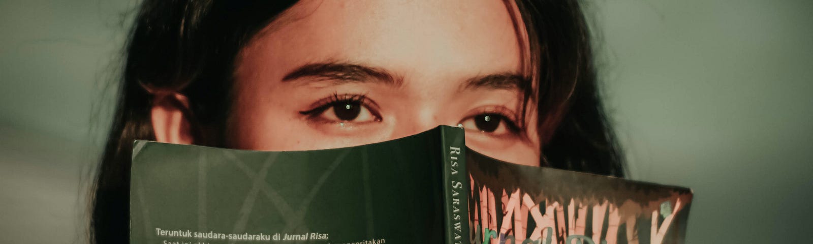 A woman looks off into the distance, covering up half her face with a book.
