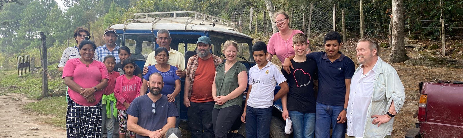 A group of adults and children pose for a photo in front of an offroad vehicle on a woodland track in Honduras