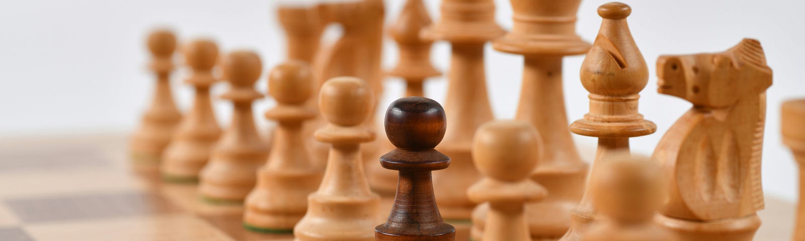 Black pawn on a chessboard surrounded by white pieces