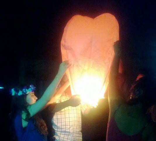 Three people lighting an orange sky lantern at night