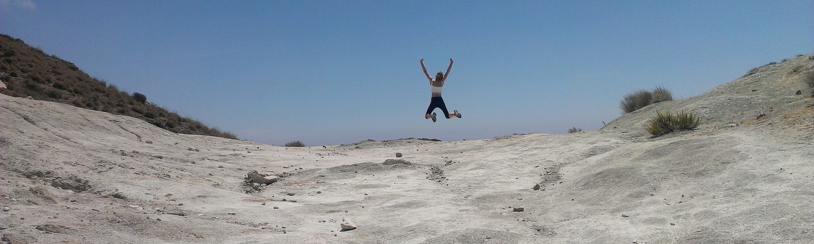 A woman jumps out of joy on a sandy trail along the beach.