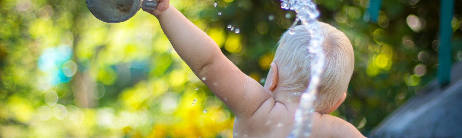 Baby sitting inside a blue plastic tub throwing a cup of water behind him.