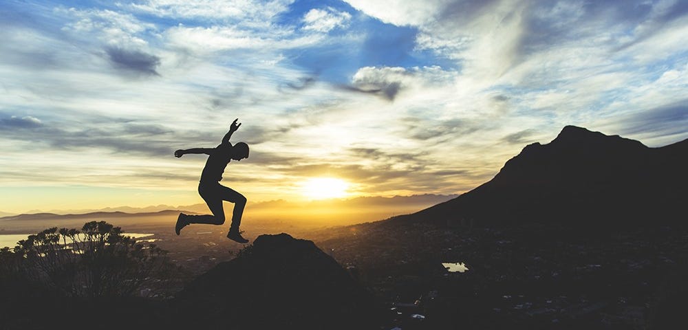 man jumping with mountains and sunrise as the background