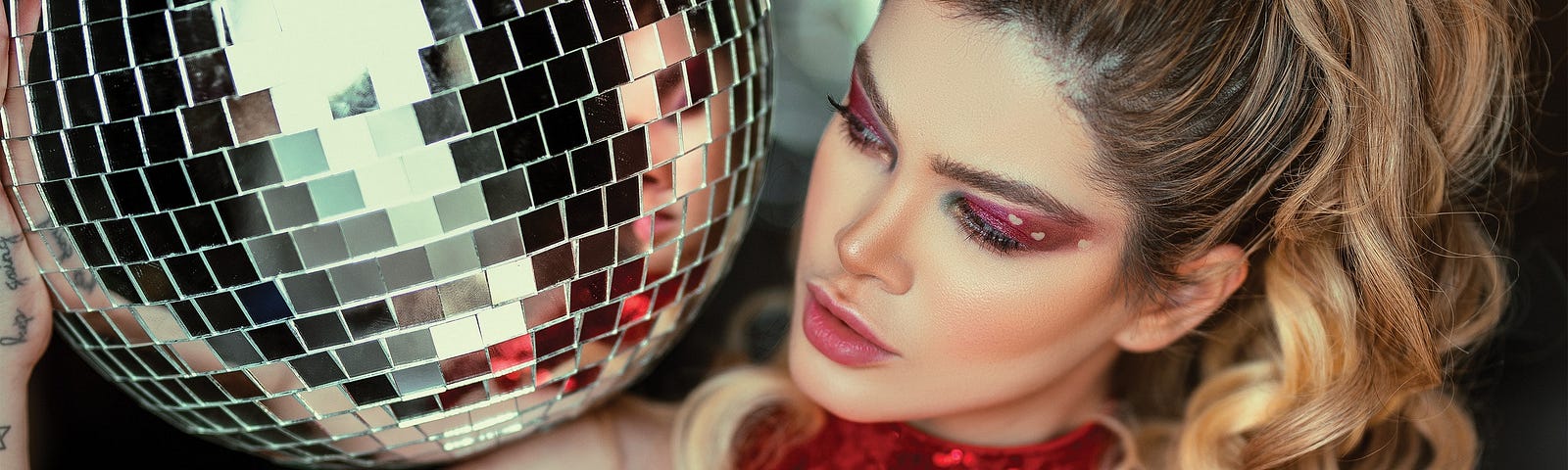 Woman wearing a red glitter halter top holding a disco ball.