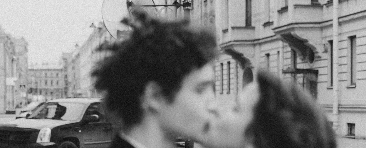 Black and white and lightly off-focus photograph of a couple kissing on the street.