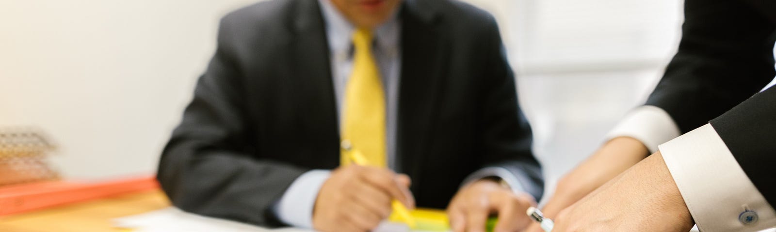 A closeup of a nameplate on a desk that reads, “I’m kind of a big deal”. Two men work in the background of the photo.