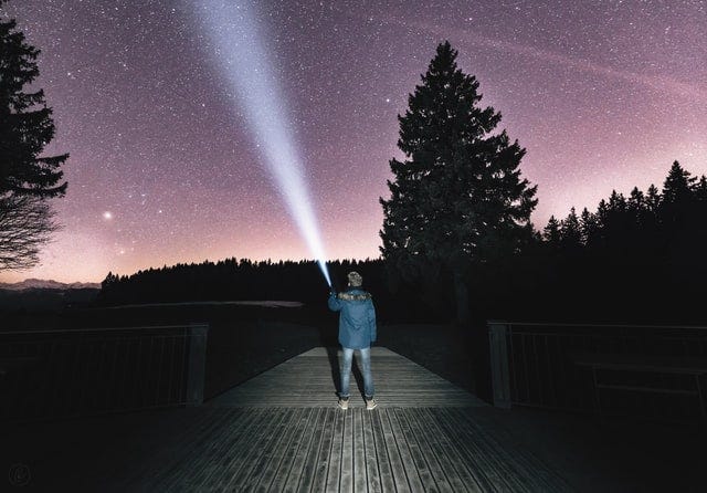 A person shining a flashlight into the night sky looking for something.