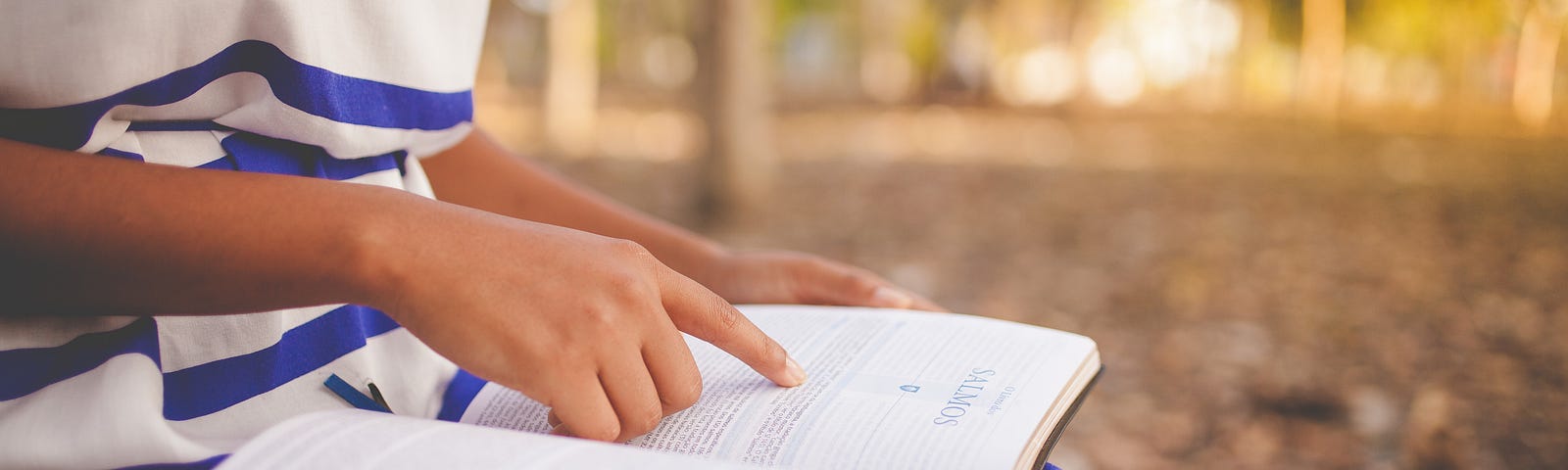 A Bible resting open on a child’s lap, as the child follows the words with their forefinger.