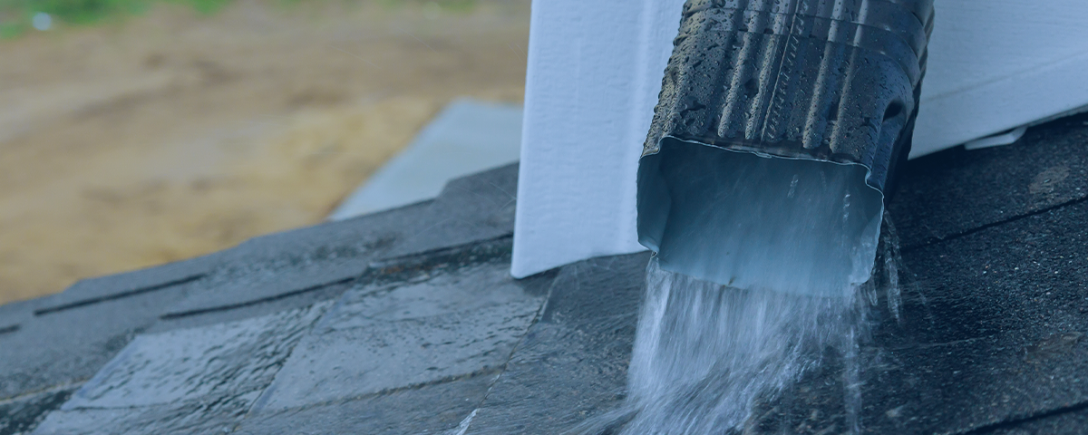 Picture showing rainwater pouring out of a gutter down pipe onto a lower rooftop