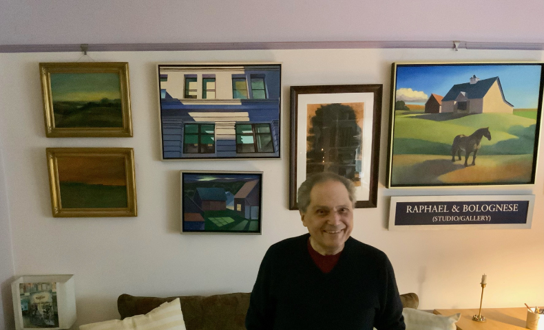 Don Bolognese standing in front of some of his artwork on the wall.