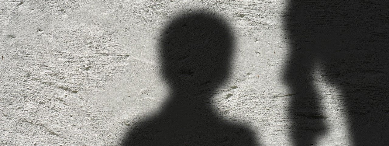 IMAGE: On a white wall, the shadow of a kid holding an adult’s arm