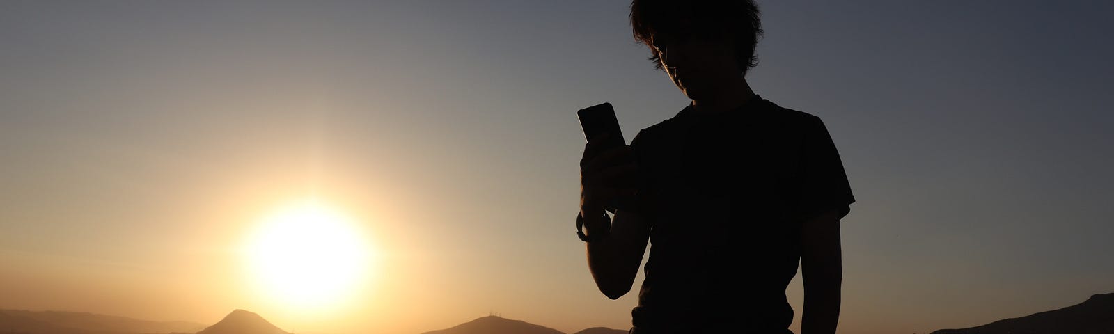 silhouette of a man looking at his phone instead of the sunrise behind him