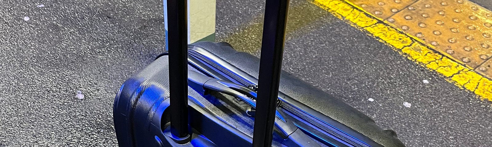 A black suitcase with a rainbow belt at a train station in England