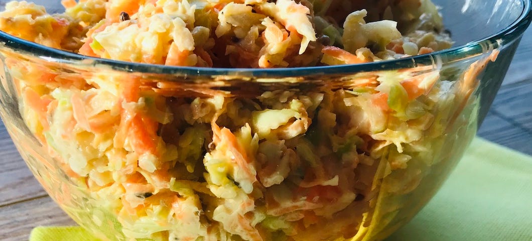 A closeup of a clear glass dish filled with coleslaw, placed upon 3 green, orange and yellow napkins