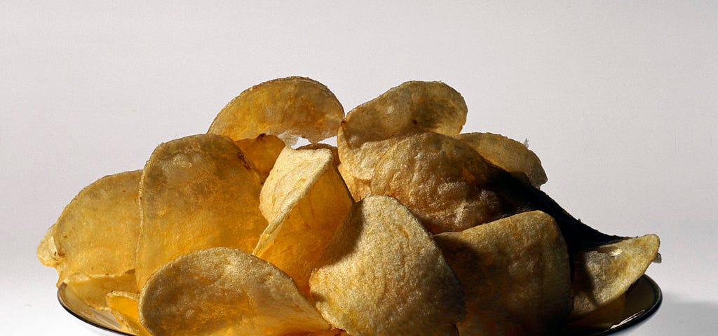 A dish overflowing with potato chips on a white background.