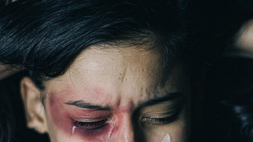 A woman beaten, with a raw wound over her right eye and taoe across her lips.