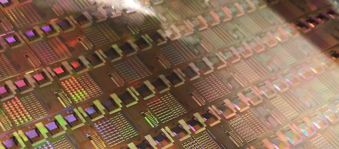 A shiny silicon wafer with many repeating patterns and rainbow coloration on it.
