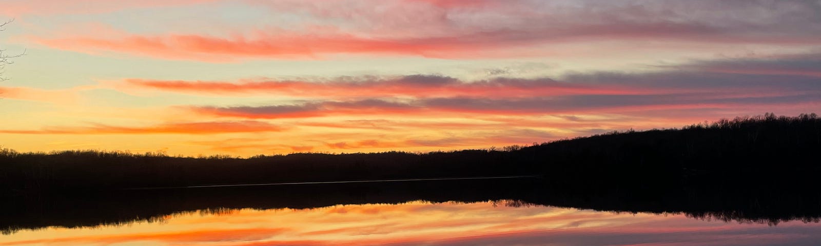 Sunset over a small lake in Wisconsin with pinks, oranges, and yellows reflected in the sky and calm water