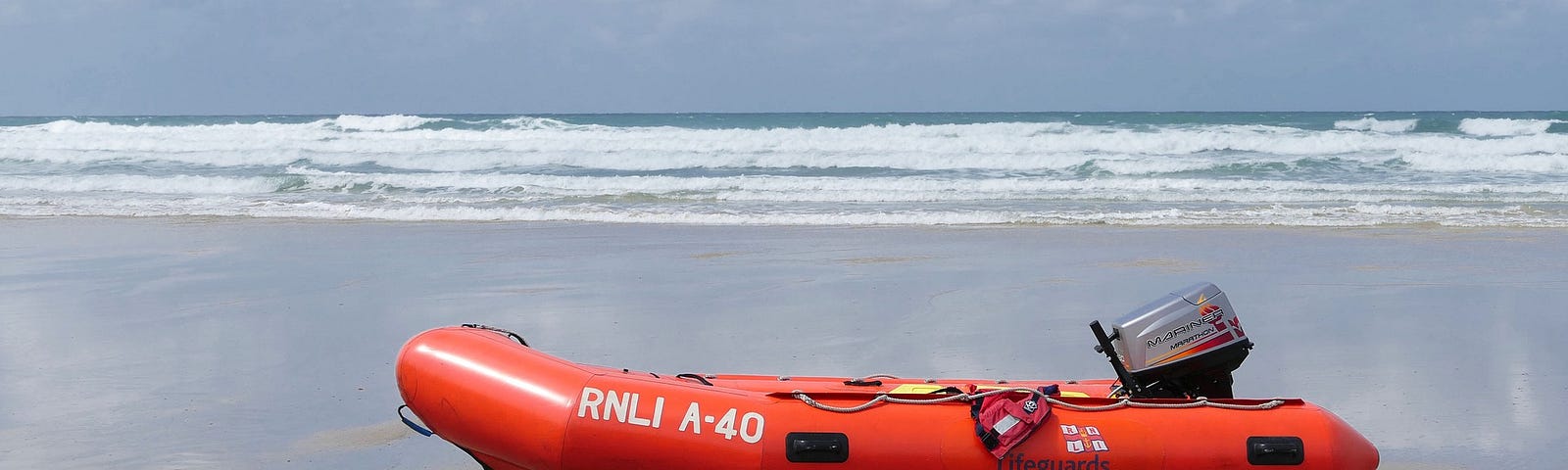 An orange lifeboat sitting in a cloudy beach.