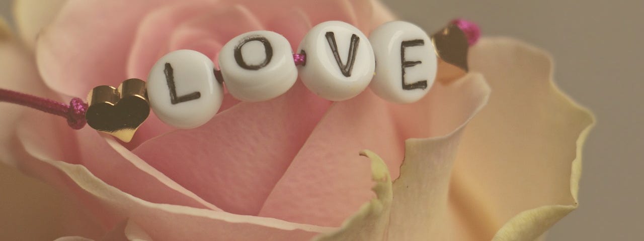 A pal pink rose and draped across ot is a bracelet spelling outvthe word love in white beads.