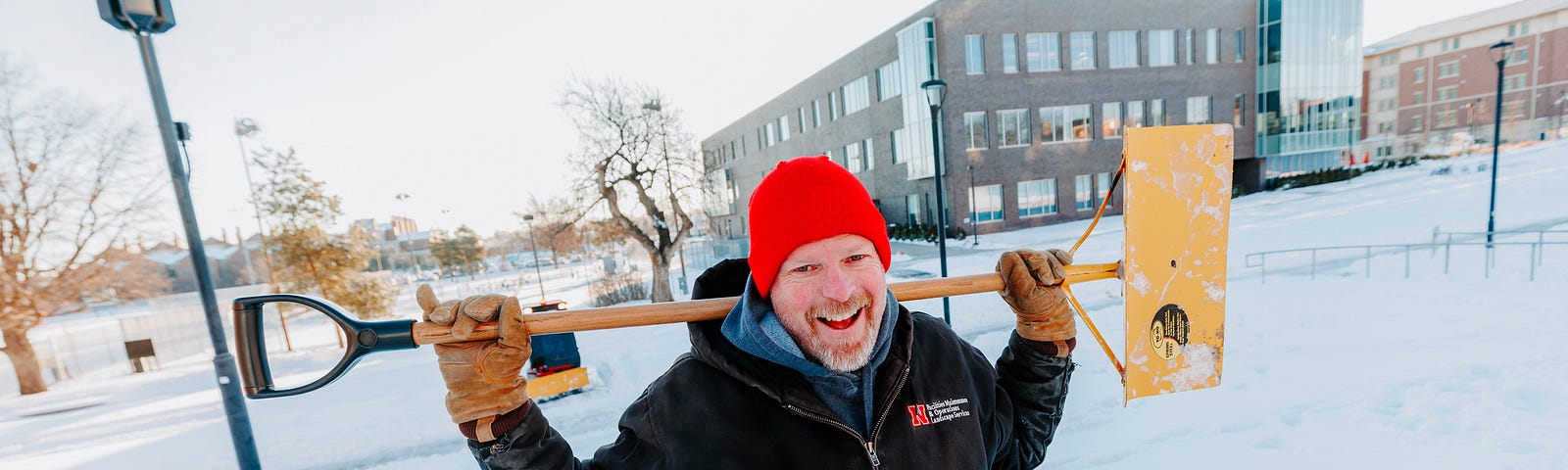 Kevin smiles for a photo while he holds a snow shovel across his shoulders
