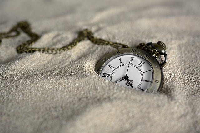 A pocket watch half buried in some sand