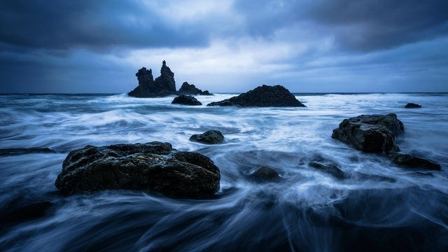 A rocky shoreline with rocks and fog at night.