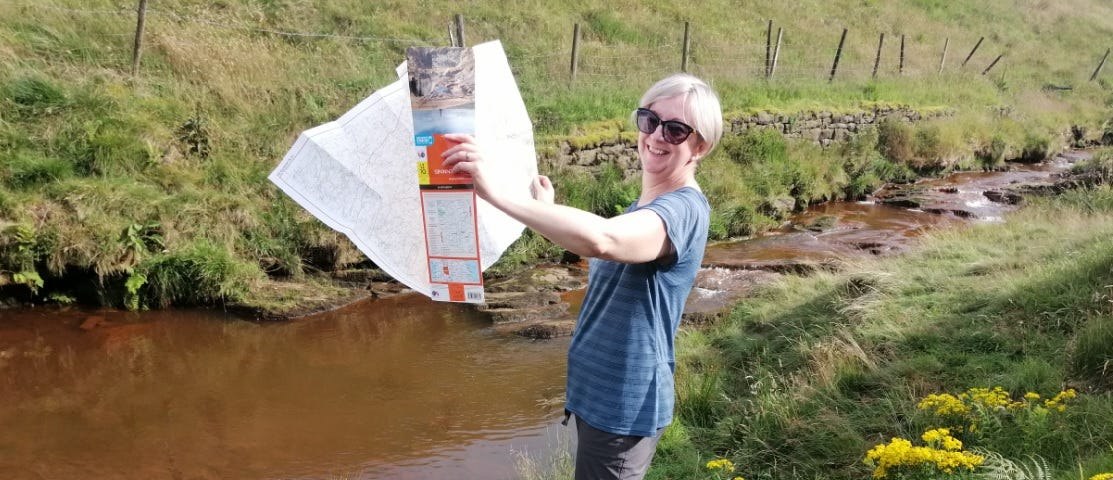 Photograph of the map curator in a field, unfolding an Ordnance Survey map