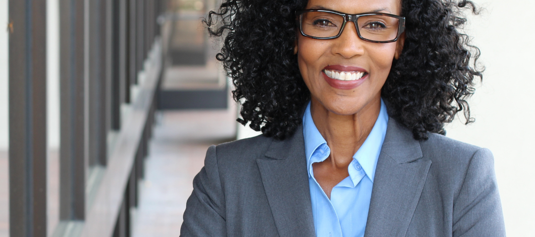 a woman in a suit looks at the camera with a confident smile and her arms crossed