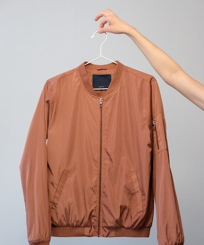 Camel coloured zip front jacked held on a clothes hanger