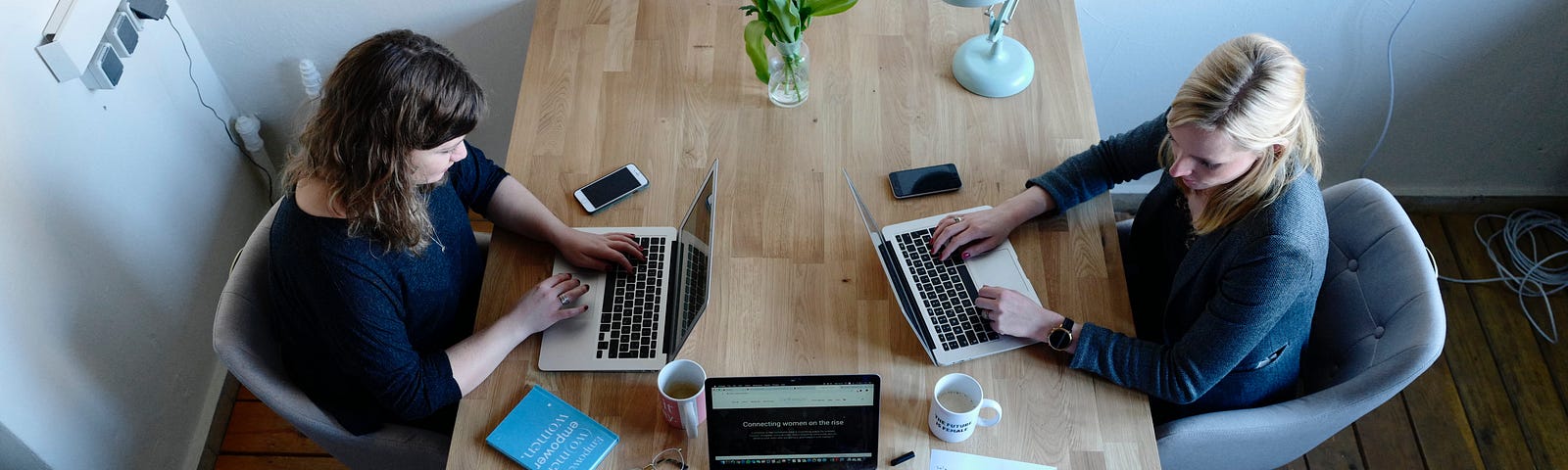 3 women with laptops sitting around a table