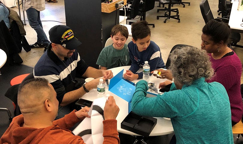 Veterans and families seated around a table, opening robot kits at our Battle of the Bots event in January 2019