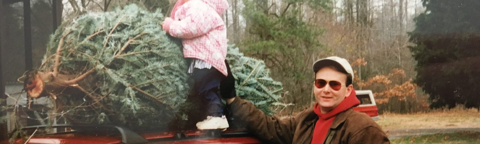 My dad loosely holds a 3-year-old me with one hand on top of the family car. I cling to a Christmas tree to keep from falling. He looks proud.