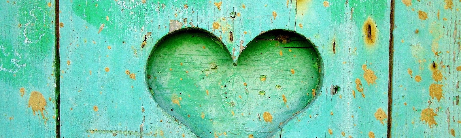 a weathered greenish blue fence with a carved heart in the center