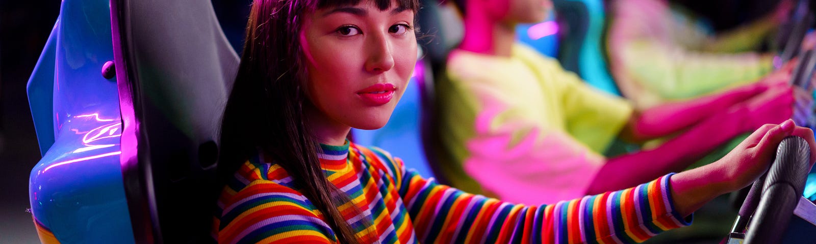 A woman in a colorfully-striped sweater plays a racing game at an arcade