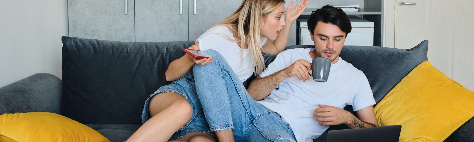 One partner drinks coffee and stares at their computer, while the other leers over them — upset with their hands spread wide.