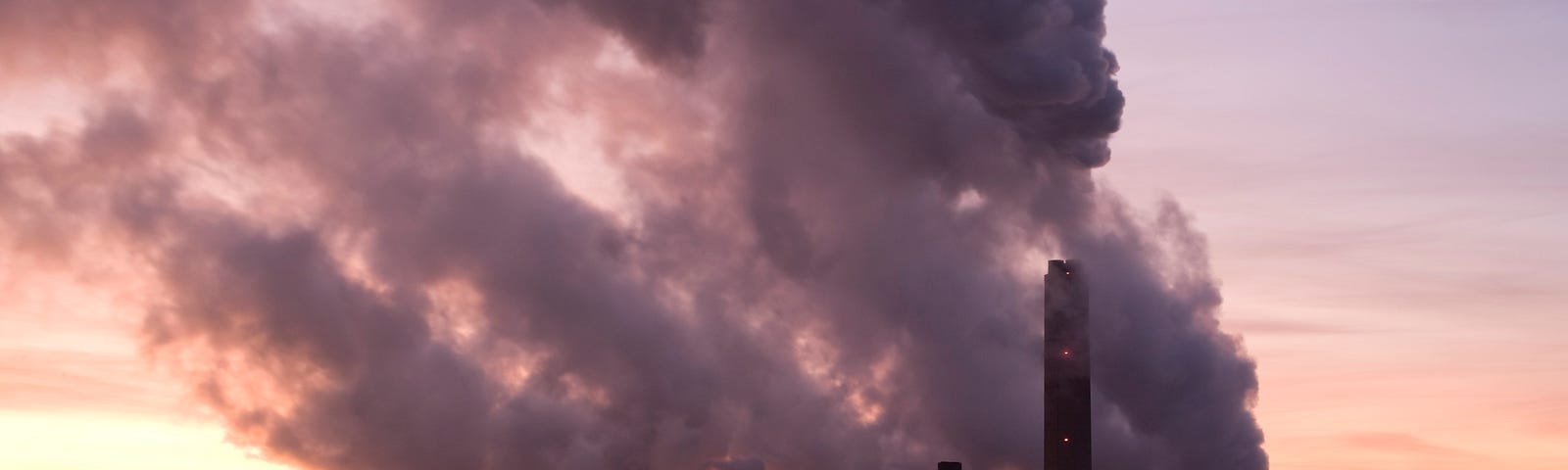 A coal-fired power plant billowing gases into the sky at sunrise