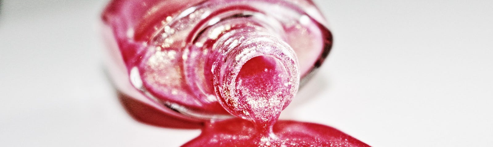 container of dark pink nail polish spilling out onto white counter