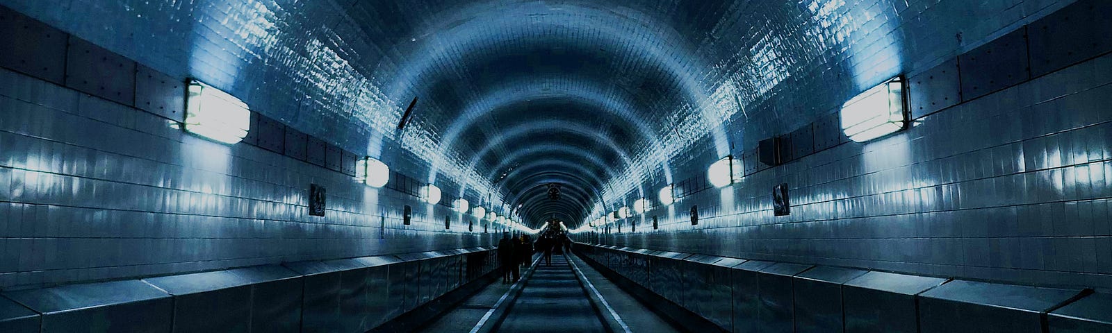 Track-level view of a subway tunnel perspective receding into the distance, with perimeter lights along the path