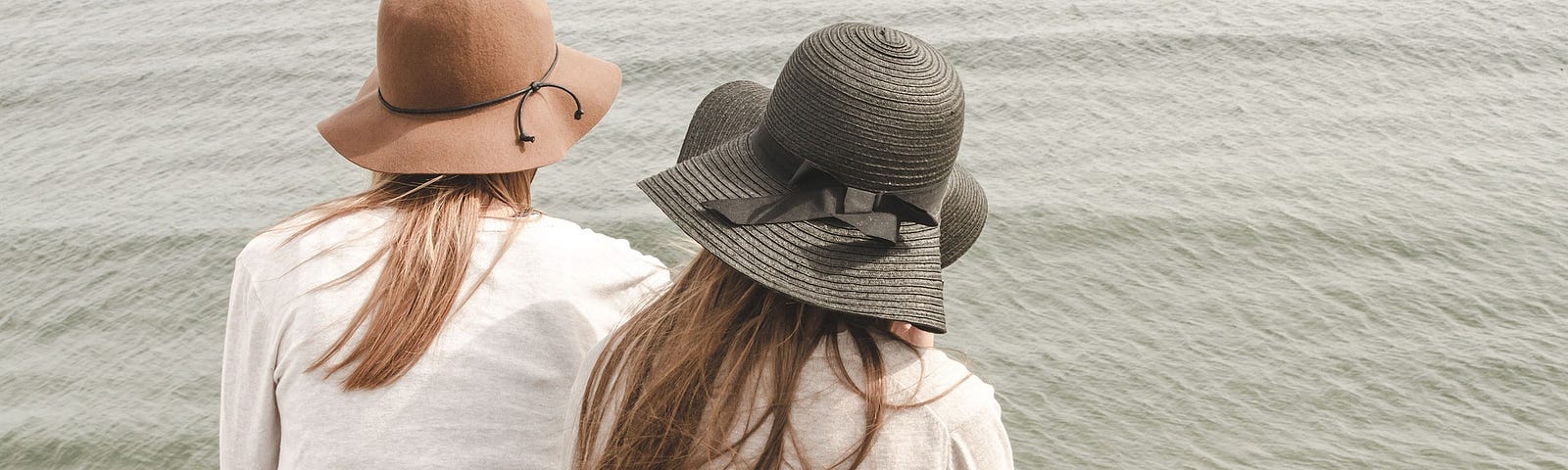 Decorative image: Two friends wearing sunhats sitting by the beach facing the water