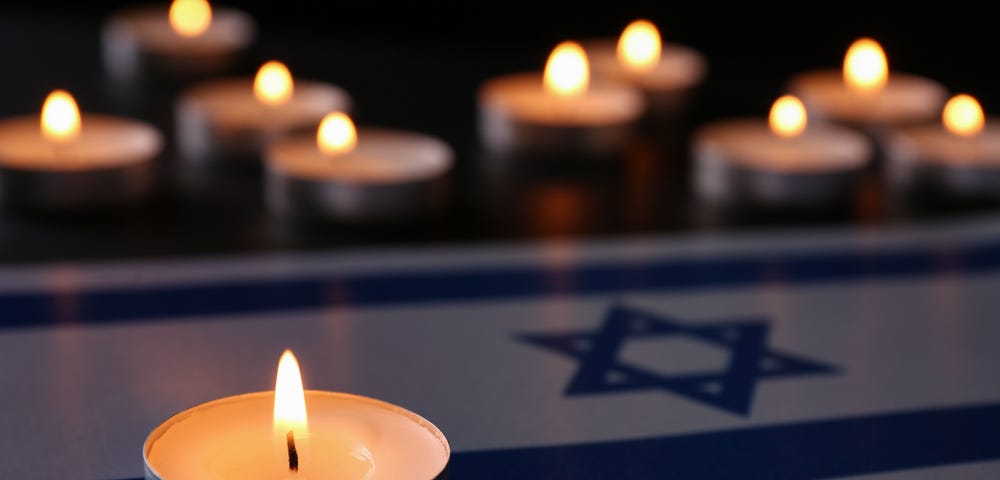 Burning candle and flag of Israel on black table. Holocaust memory day