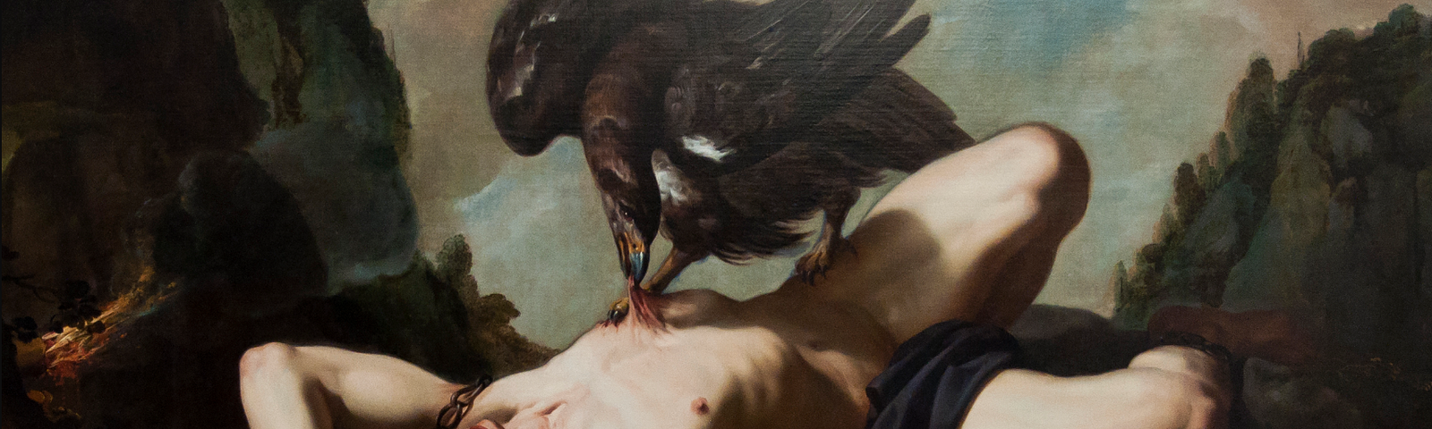 A light-skinned man lies naked, prone on a rock. His arms are bound with chains, and his mouth is open in a yell. A large, black bird stands on top of him, biting at his abdomen with its beak.