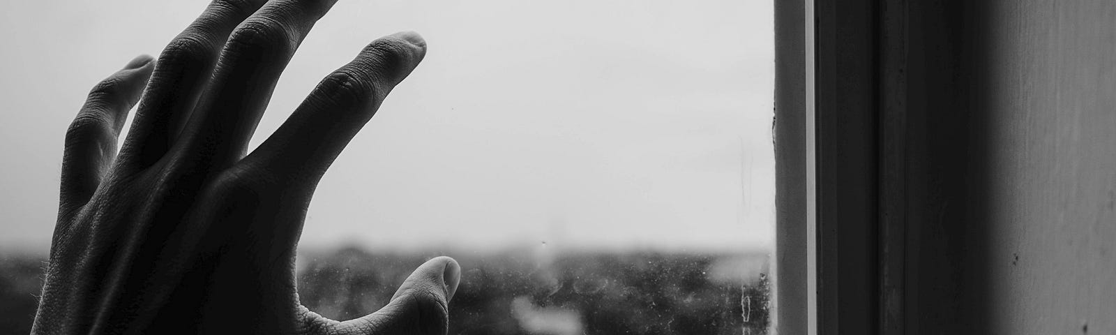 A stark and bleak black and white photograph of a hand touching a window pane.