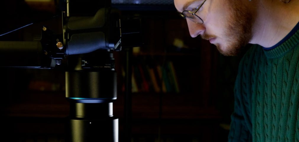 Alex, wearing a green jumper and purple gloves, photographing a quarter-plate glass negative placed on a light sheet