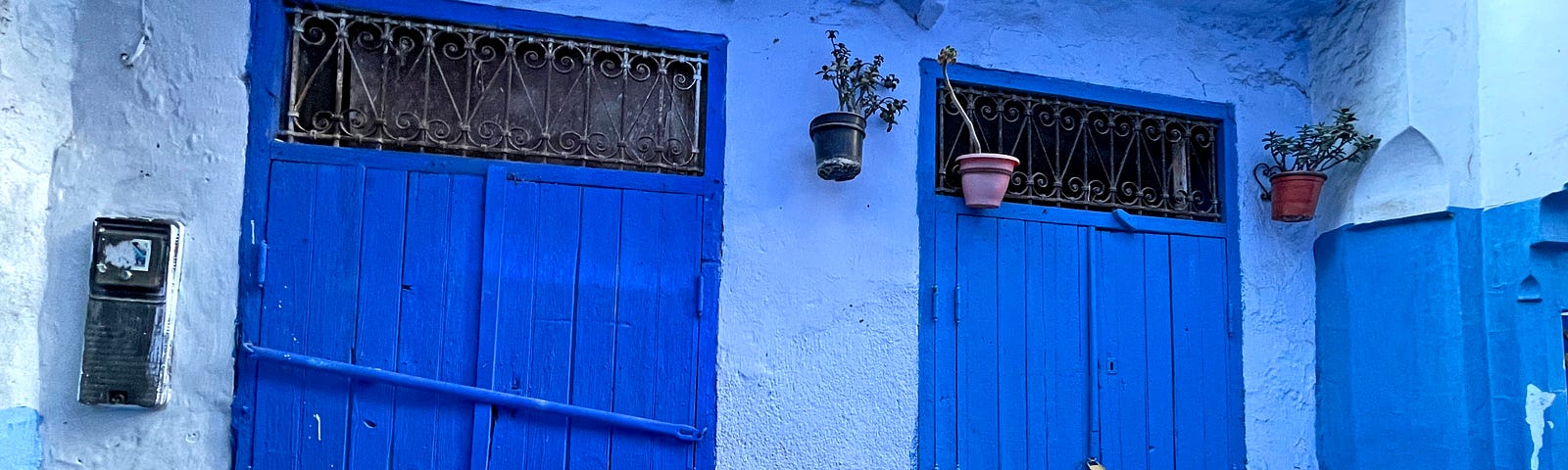 Exterior of a home painted baby blue with darker blue shutters on a window and on the double doors to the home.